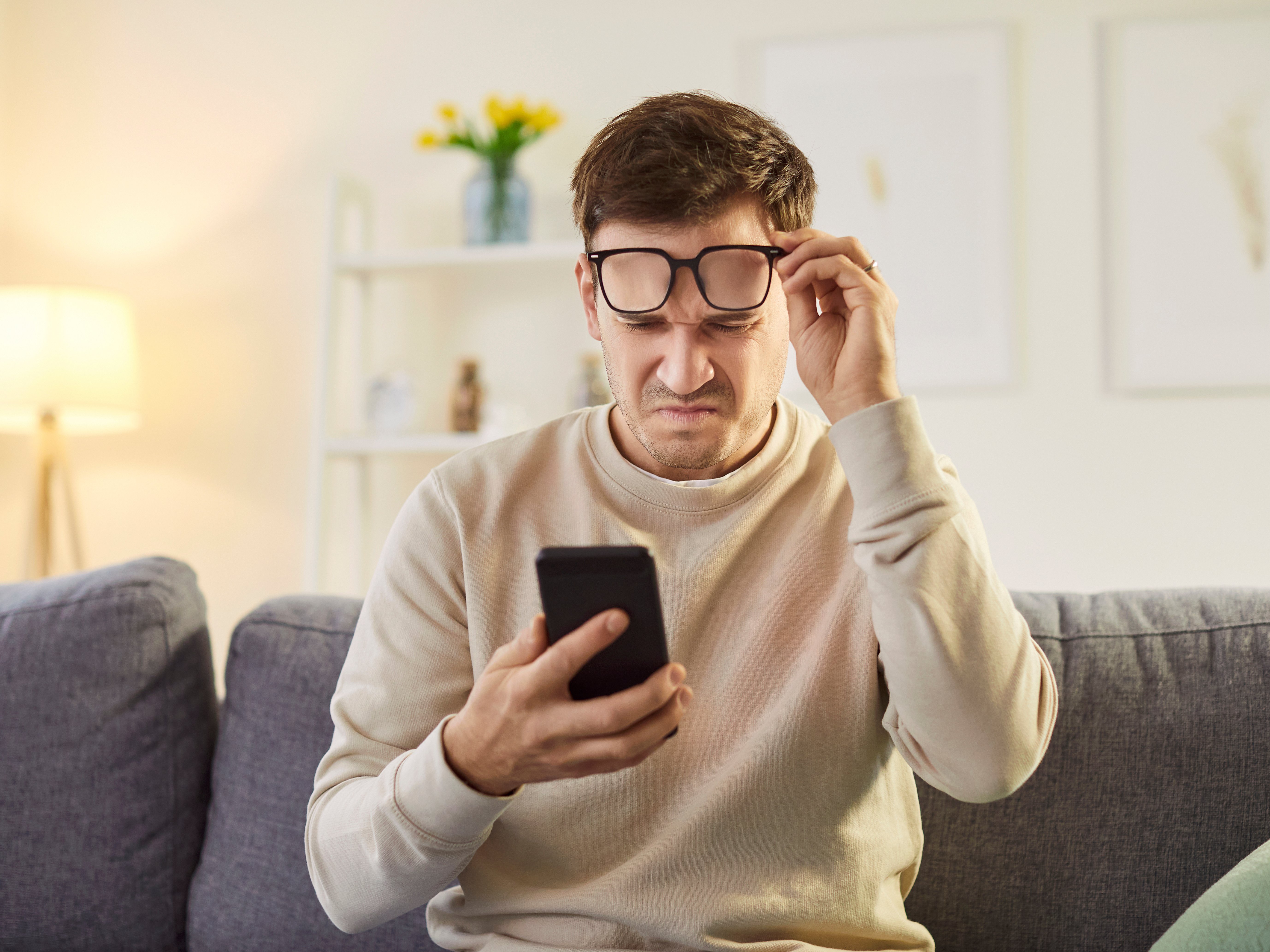 Mann hebt Brille, kneift die Augen zusammen und versucht etwas, auf seinem Smartphone zu lesen